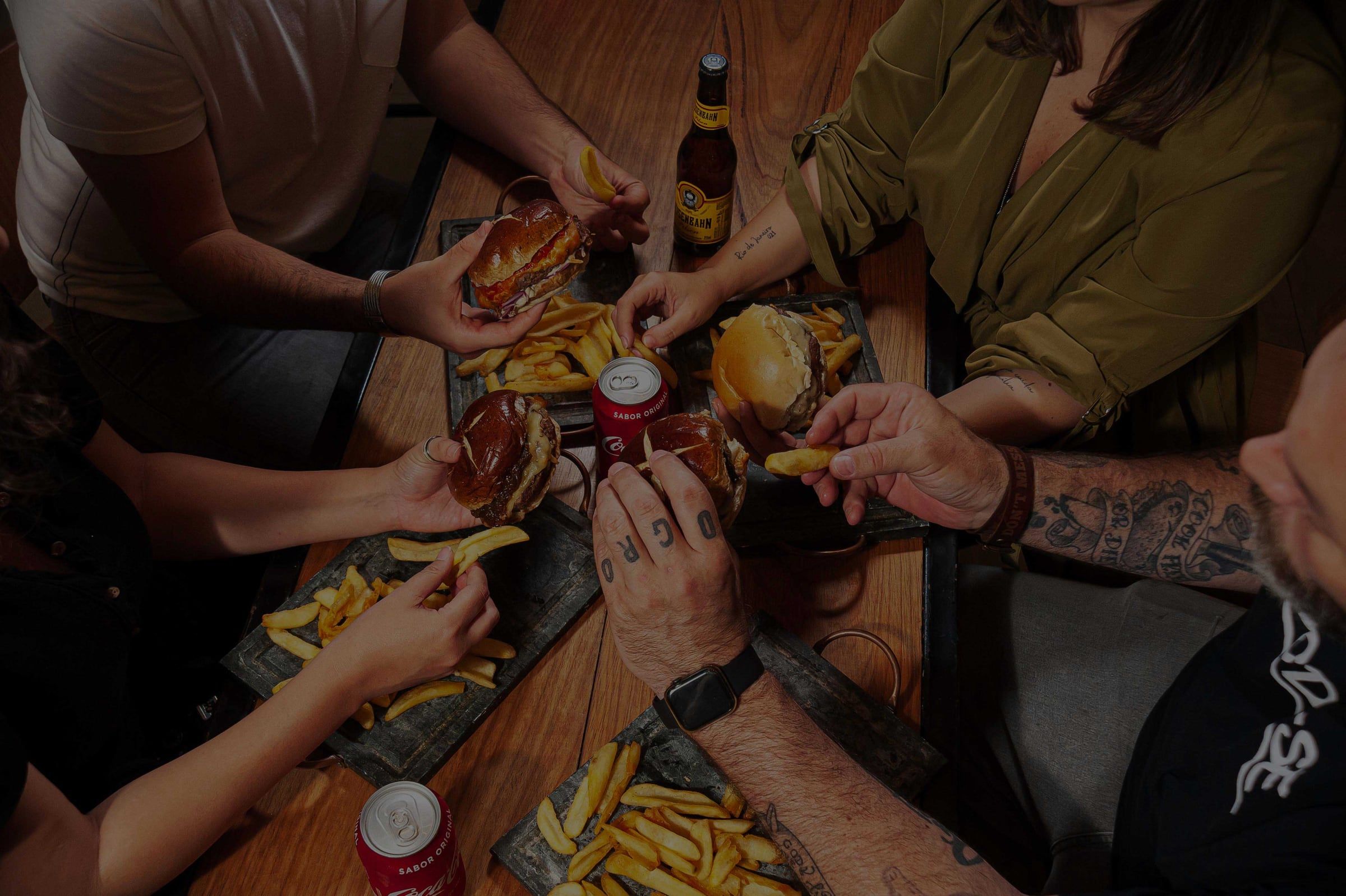 Mãos dividindo hambúrgueres e fritas numa mesa