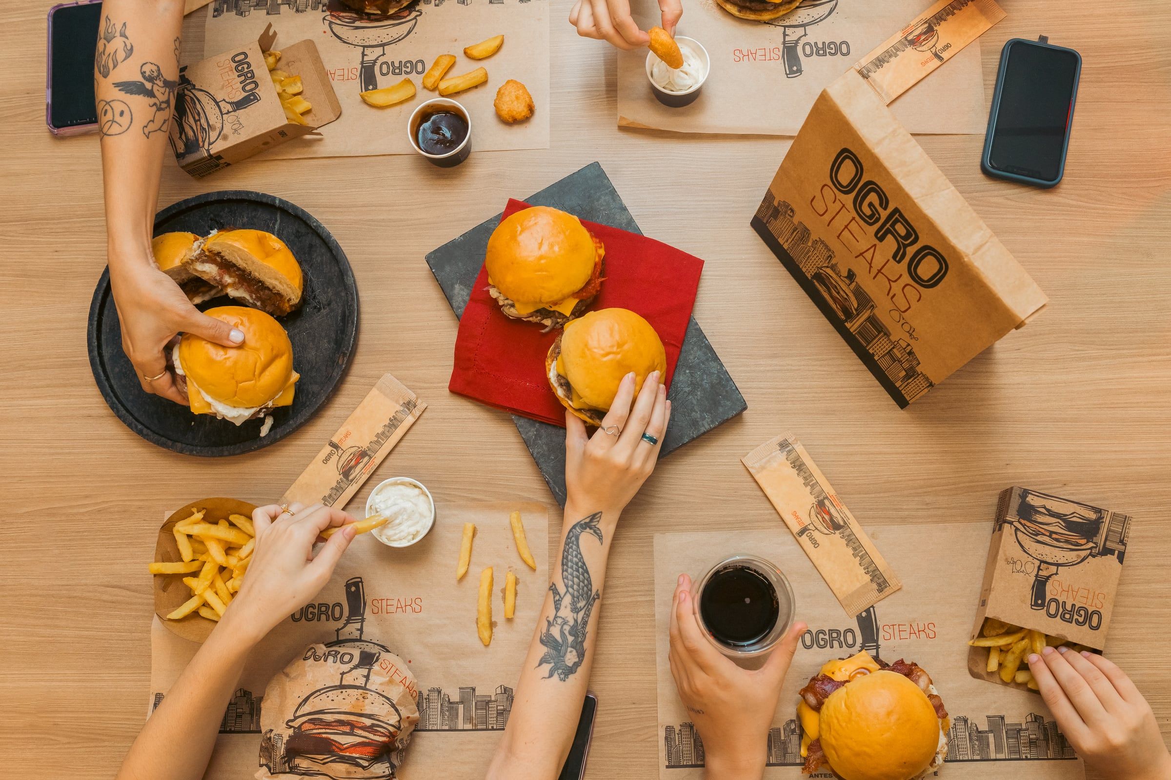 Mesa vista de cima com hambúrgueres, fritas e as embalagens da Ogro Steaks