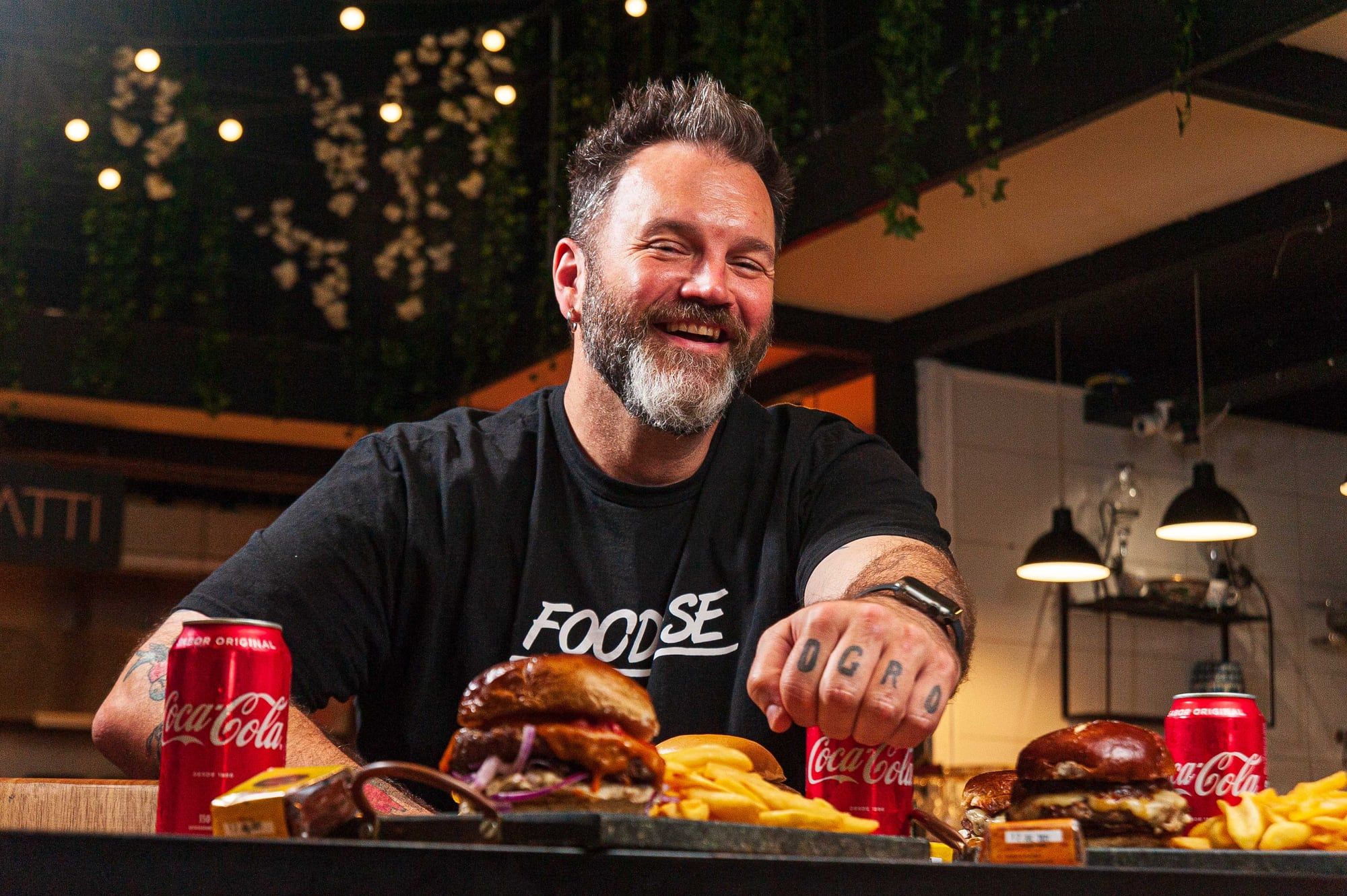 Jimmy McManis sorrindo à mesa com hambúrgueres da Ogro